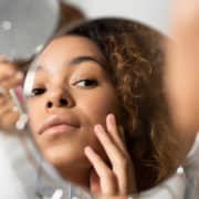 Afro Woman Looking In Mirror Touching Face At Bathroom