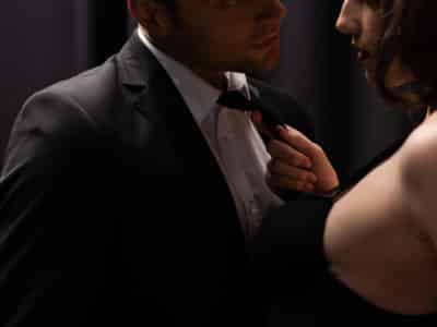 cropped view of seductive woman pulling tie of man in suit on black
