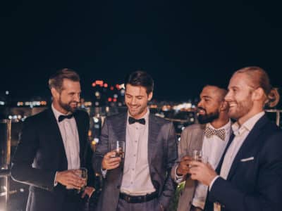 Group of handsome young men in suits and bowties drinking whiskey and smiling