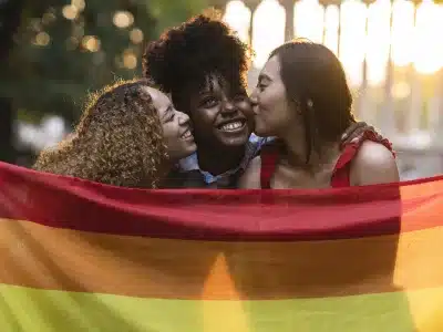 group of multiracial female friends with lgbt rainbow flag hugging at sunset jpg